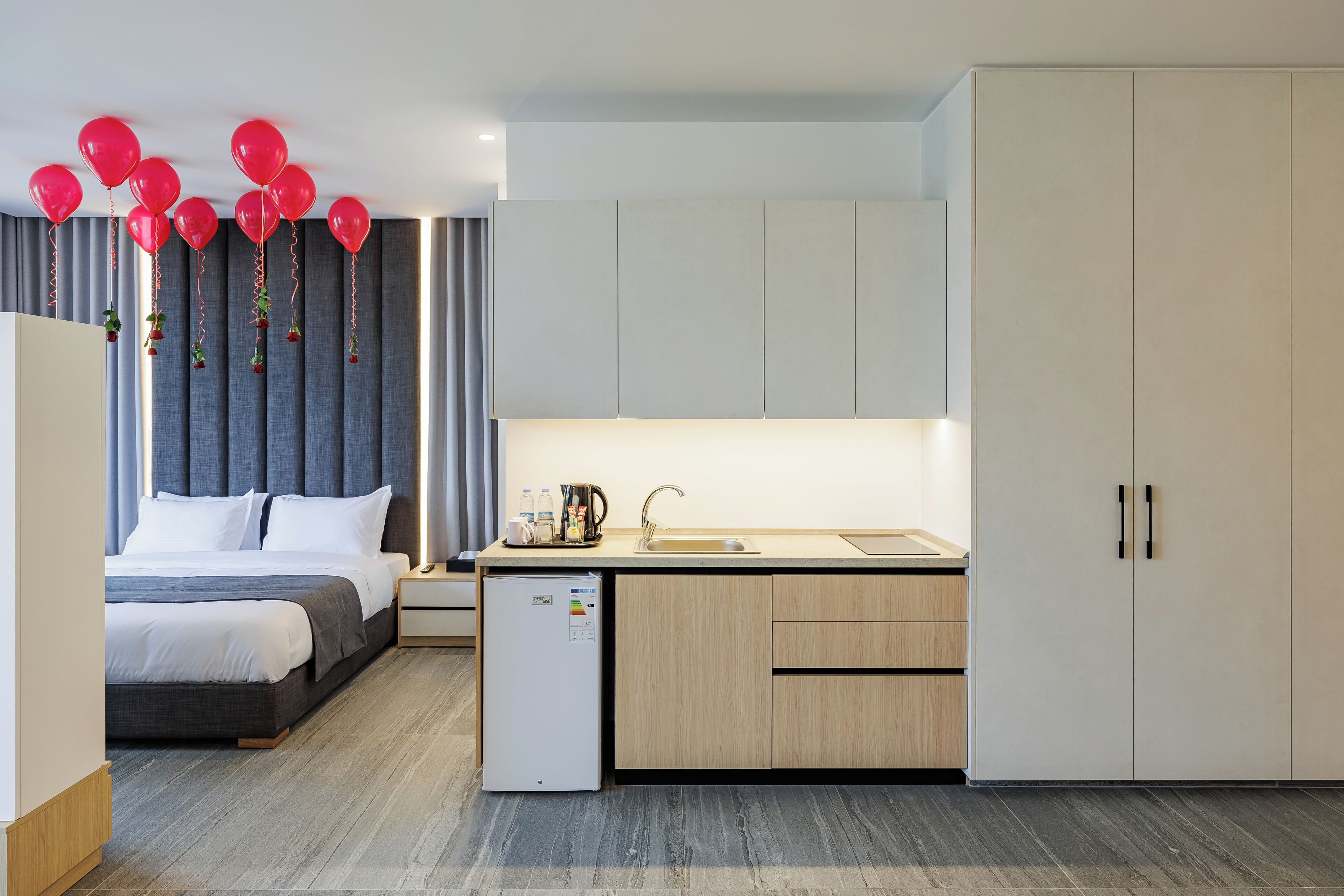 A modern hotel room with a bed, a small kitchenette, and a large wardrobe.