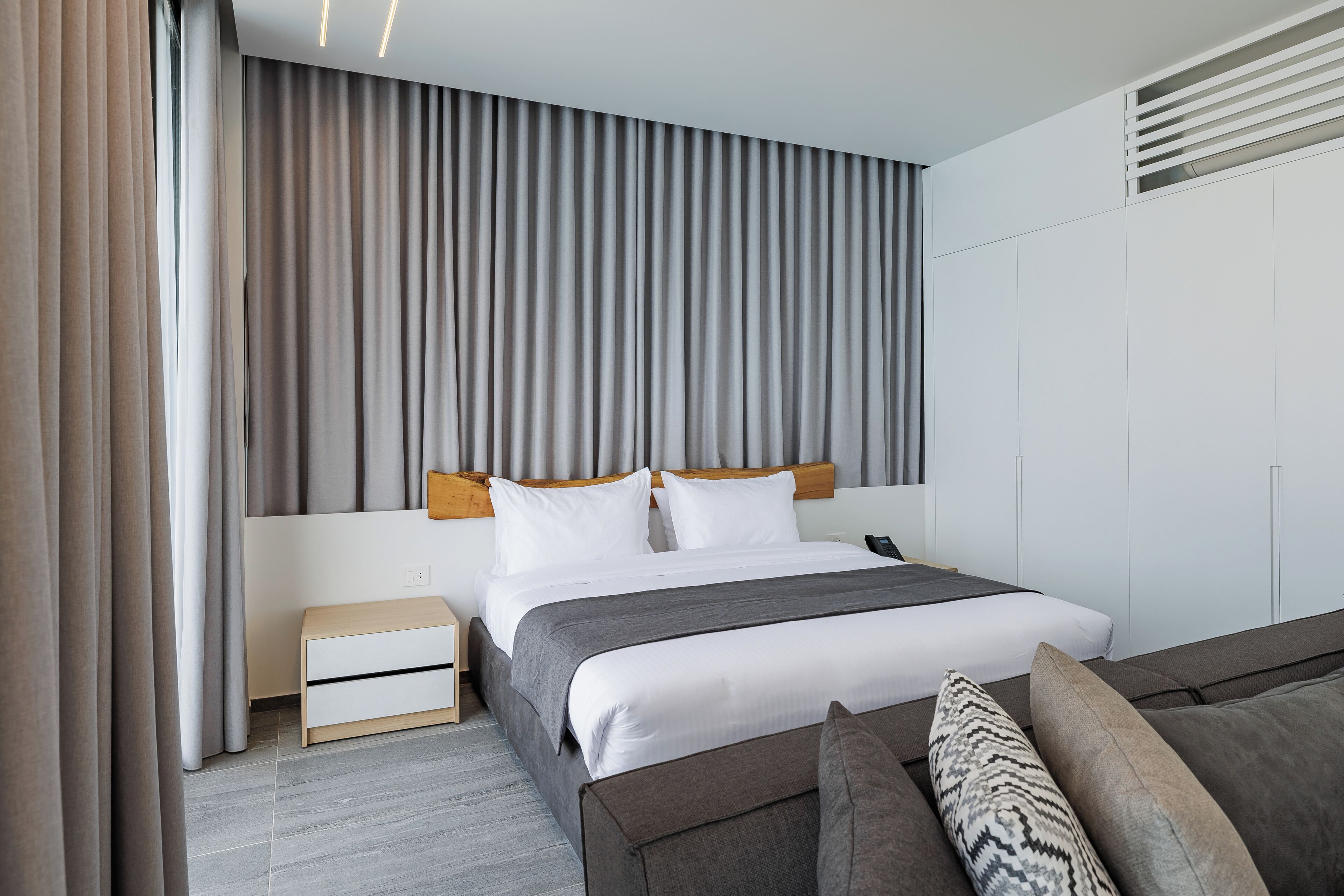 A modern hotel room with a neatly made bed, a bedside table, and a sofa.
