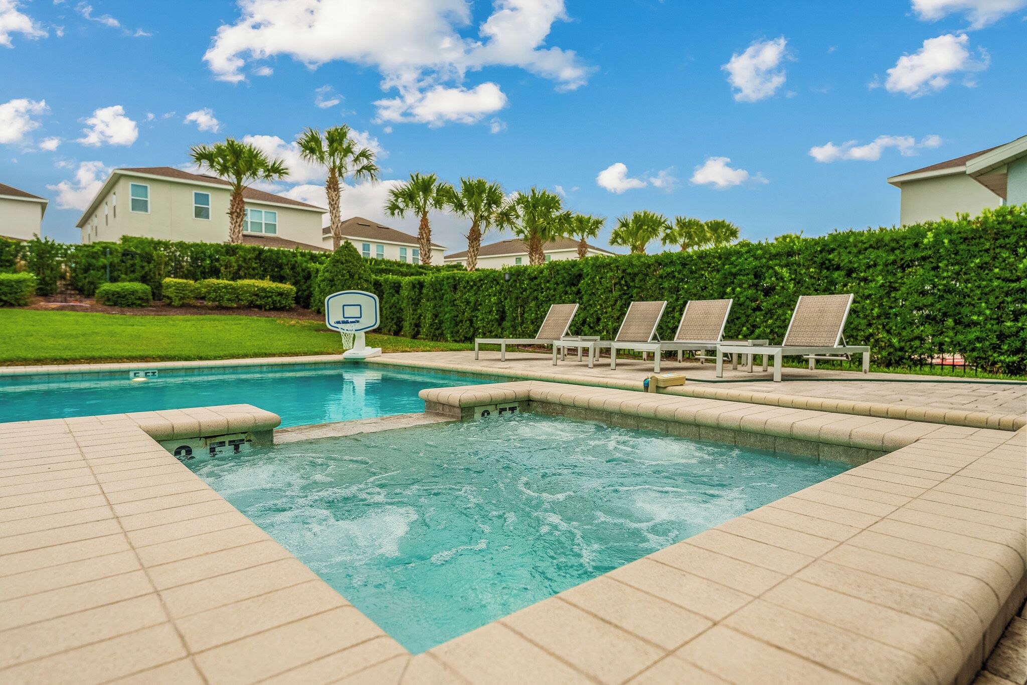 A swimming pool with a hot tub, lounge chairs, and a basketball hoop.
