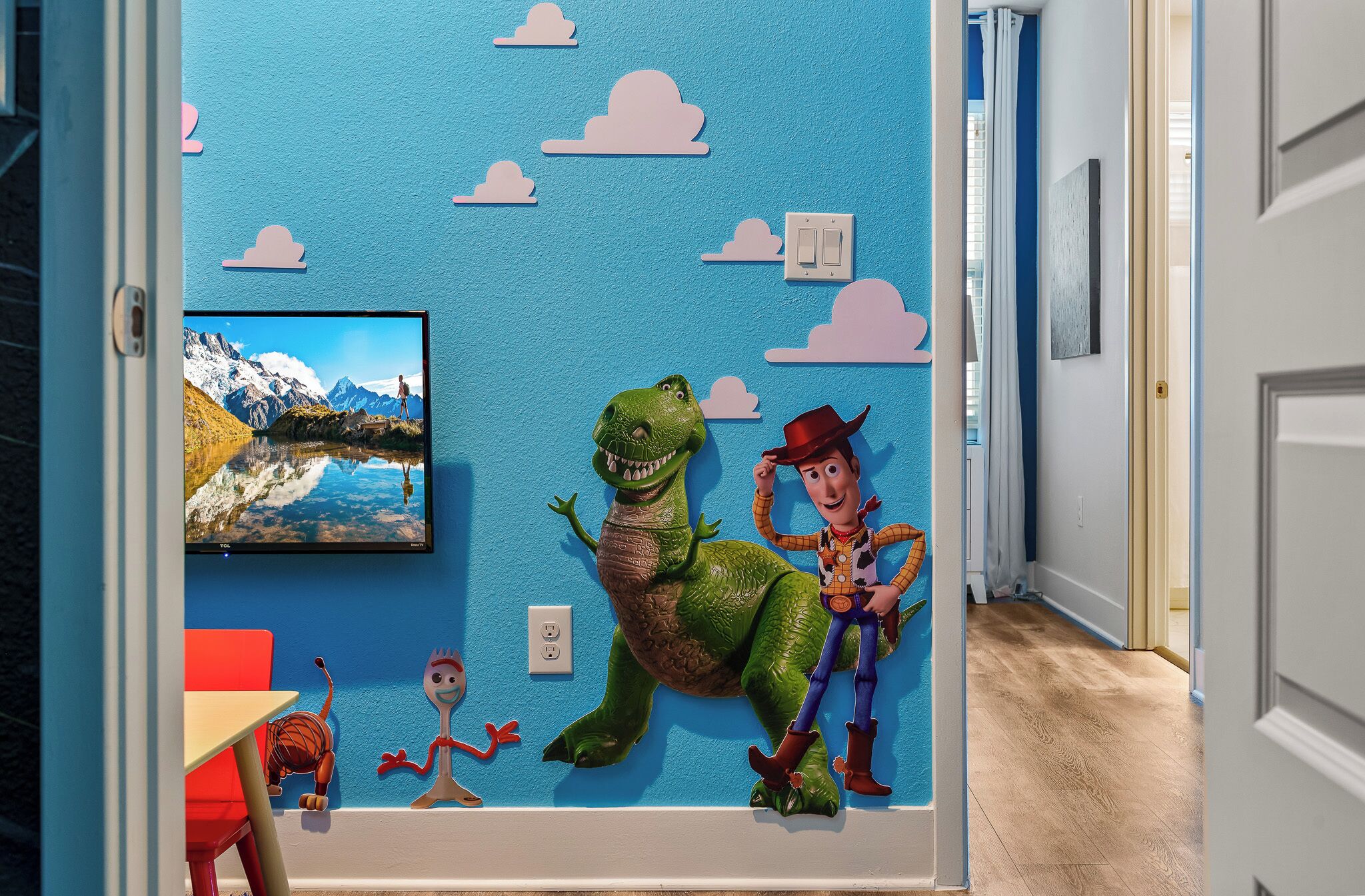 A room with a blue wall, a mounted TV, and a dinosaur and cowboy toy.