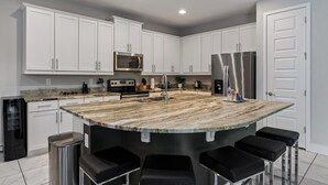 A modern kitchen with white cabinets, stainless steel appliances, a granite countertop, and a bar area with stools. - 5BR Gorgeous Villa • Spiderman • Near Disney (Kissimmee)