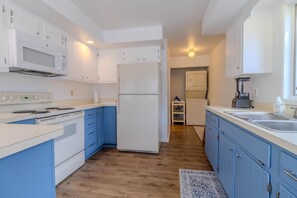 Modern kitchen with a white microwave, refrigerator, stove, and sink, set against blue cabinets and a wooden floor.