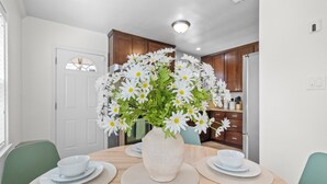 Ein Esstisch mit einer Vase voller weißer Blumen, umgeben von Tellern und Schüsseln, in einem Raum mit Holzkästen und einer weißen Tür.