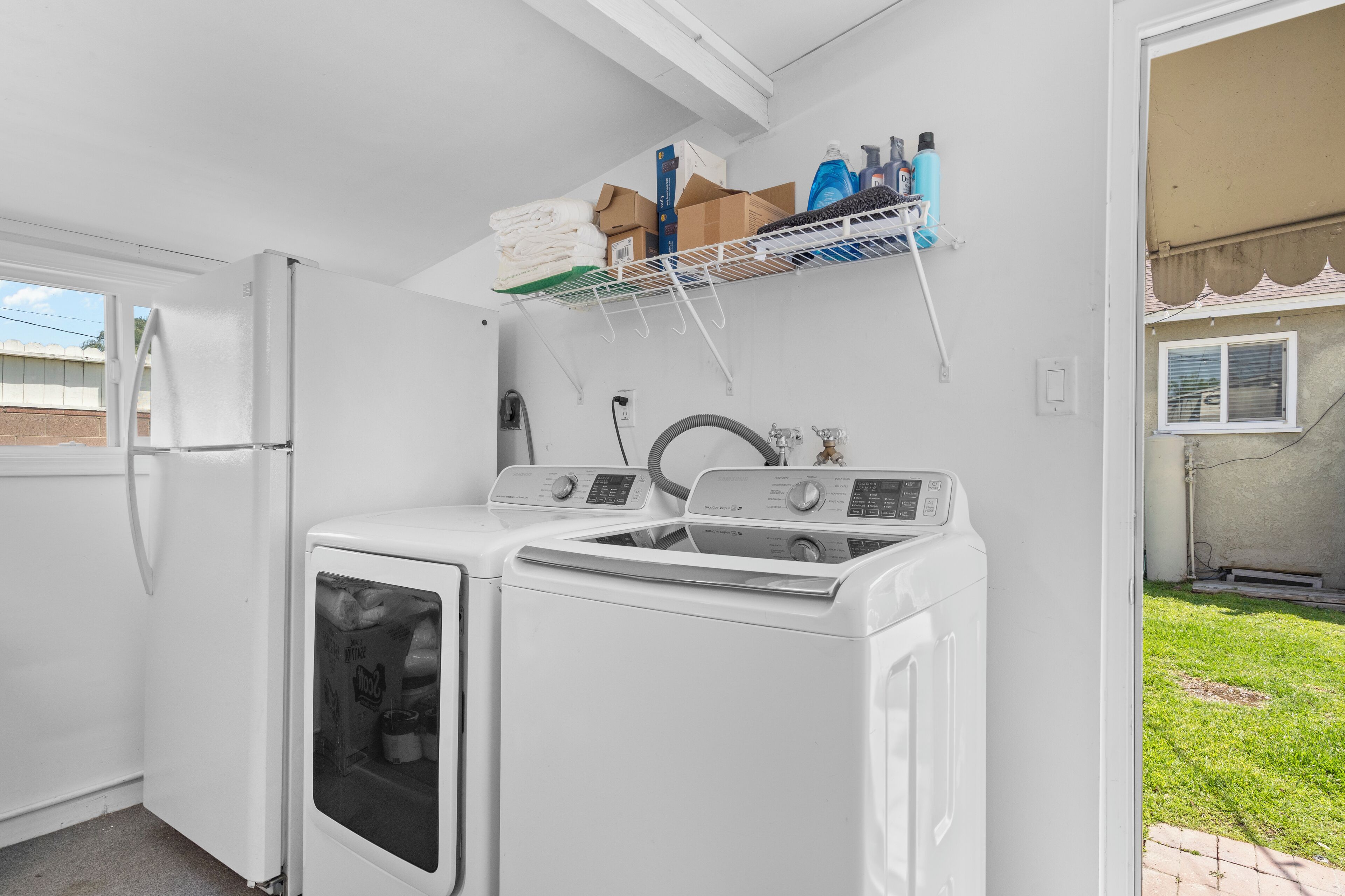 Un área de lavandería con lavadora y secadora, un estante con productos de limpieza y una ventana al exterior.