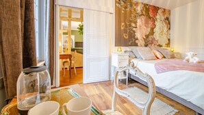 A bedroom with a bed, bedside table, lamp, and a floral wall mural. - L'Ecrin de la Cathédrale (TROYES)