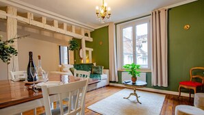 A dining area with a wooden table, white chairs, and a chandelier. There is a sofa with a green cushion and a potted plant. - L'Ecrin de la Cathédrale (TROYES)