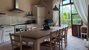 Una cocina con mesa de madera, armarios blancos, estufa y lámpara colgante.