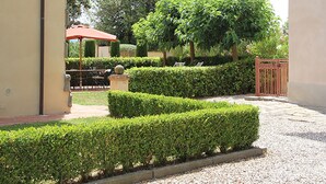 Un jardín bien cuidado con setos ordenados, un camino de grava y una sombrilla roja.