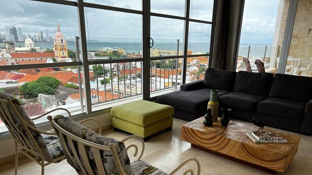 Una sala de estar moderna con un ventanal grande que da a una vista panorámica de la ciudad y el mar.