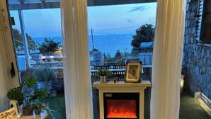 A cozy living room with a fireplace, a sofa, and a view of the sea through large windows.