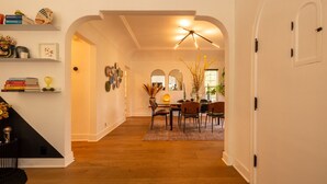 A spacious hallway with wooden flooring leading to a dining area with a table and chairs. - Hauser House, Modern Artful Spanish-style Bungalow (Los Angeles)