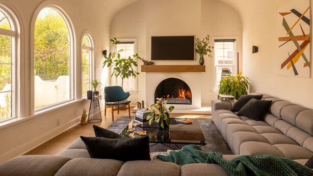 A living room with a fireplace, a sofa, a chair, and a TV. - Hauser House, Modern Artful Spanish-style Bungalow (Los Angeles)