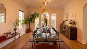A dining room with a glass table, chairs, a potted plant, and a cabinet. - Hauser House, Modern Artful Spanish-style Bungalow (Los Angeles)