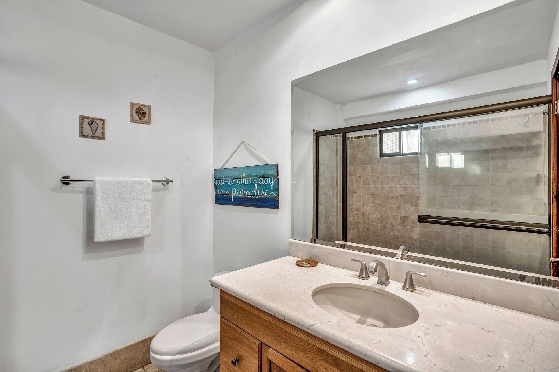 A bathroom with a white toilet, a vanity with a marble countertop, a sink, and a large mirror.