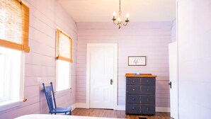 A bedroom with a bed, a dresser, a chair, a door, and a chandelier. - Sea la Vie - Margaree farmhouse by river and sea! (Margaree Harbour)