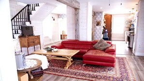 A spacious living room with a red leather sofa, a wooden coffee table, and a patterned rug. - Sea la Vie - Margaree farmhouse by river and sea! (Margaree Harbour)