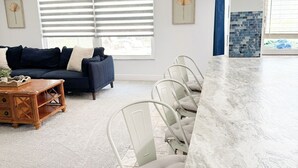 A modern living room with a sofa, coffee table, and dining area with chairs. - LE BLEU Charming Poolside Retreat/Close to beach (Bonita Springs)