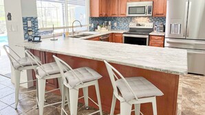 A modern kitchen with a large island, stainless steel appliances, and a view of the outdoors. - LE BLEU Charming Poolside Retreat/Close to beach (Bonita Springs)