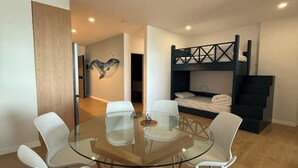 Quarto moderno com beliche, mesa de jantar de vidro com cadeiras e uma obra de arte pendurada na parede.