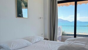 Quarto de hotel com cama, janela vista para o mar e ventilador de teto.