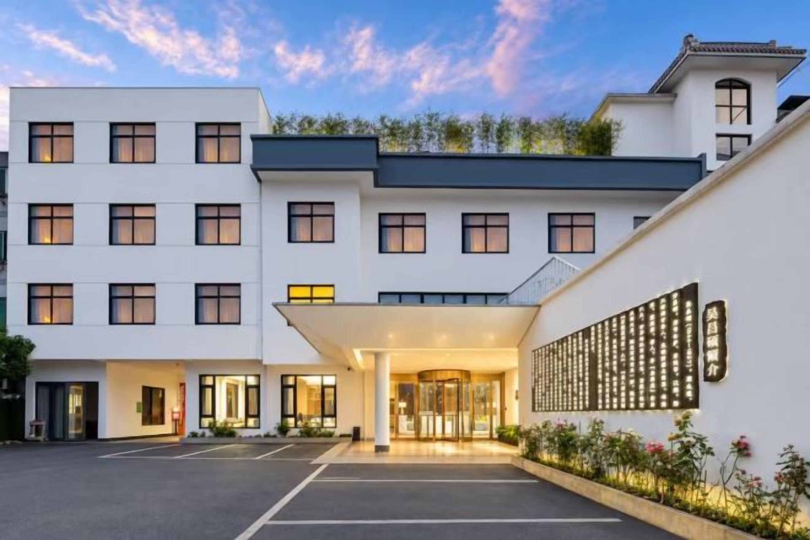 Un hotel con fachada moderna, acceso cubierto y estacionamiento.