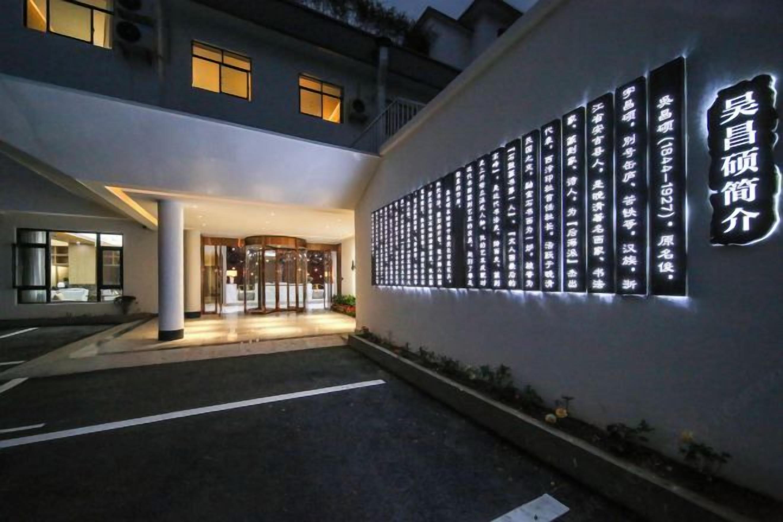 A hotel entrance with a wall of illuminated signs, a covered entrance, and a parking area.