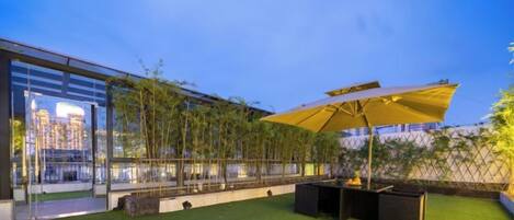 Een dakterras met kunstgras, een gele parasol en uitzicht op een stadsbeeld.