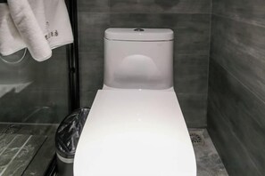 Eine weiße Toilette in einem Badezimmer mit gefliesten Wänden und einem Mülleimer.