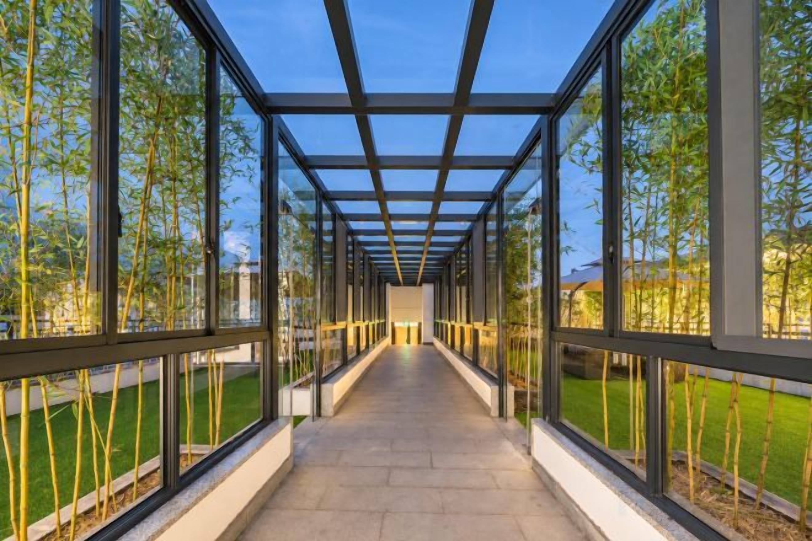 Een overdekte doorgang met glazen panelen en metalen balken, omgeven door groen.