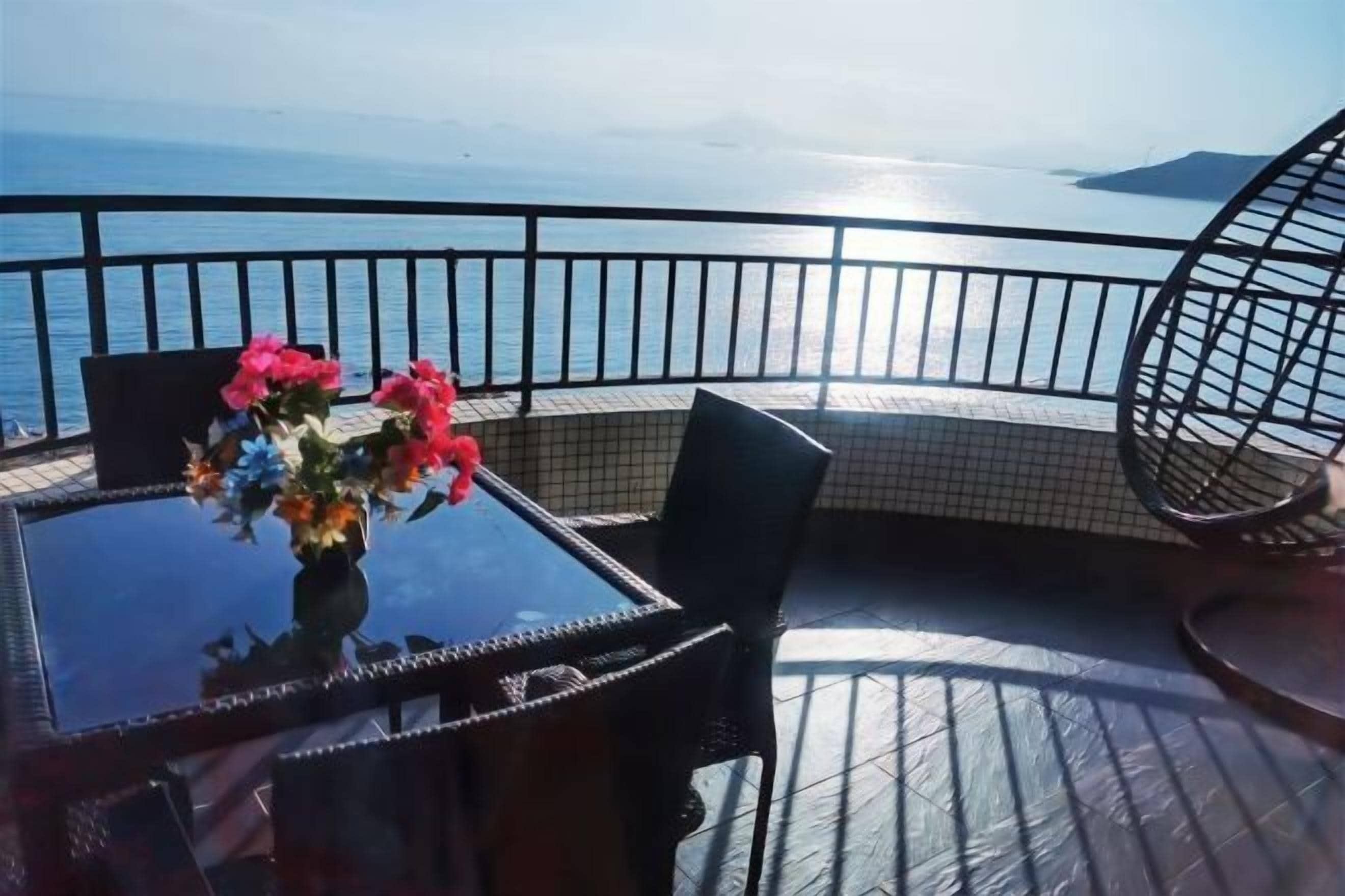 A balcony with a table and chairs, a vase of flowers, and a view of the sea.