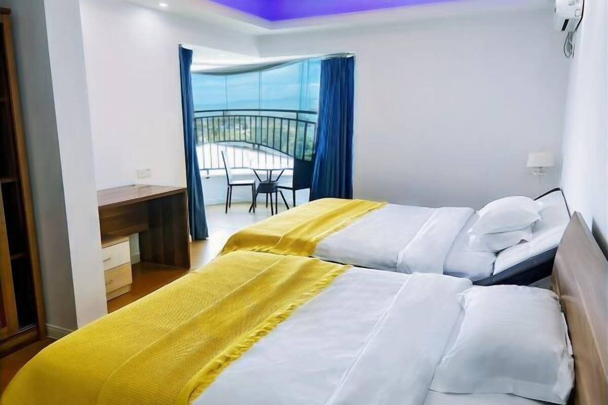 A hotel room with two beds, a desk, and a balcony with a view.