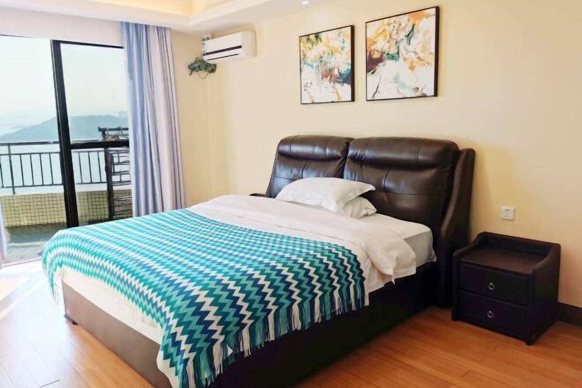 A bedroom with a bed, a nightstand, a balcony with a railing, and two wall-mounted artworks.
