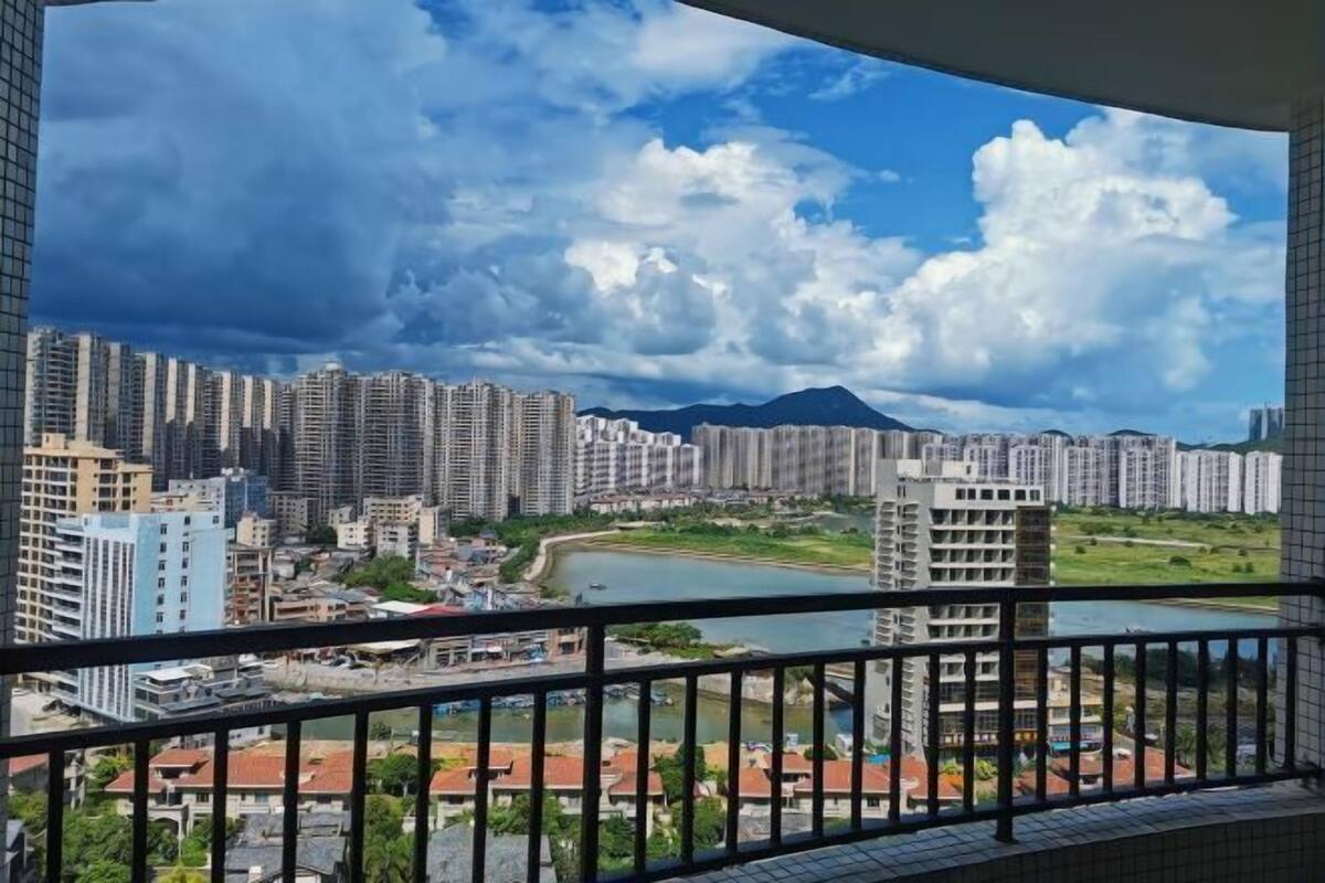A view from a balcony overlooking a cityscape with high-rise buildings, a river, and a mountain in the distance.