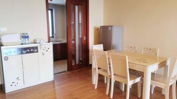 A compact kitchen with a dining table and chairs, a refrigerator, and a water dispenser.