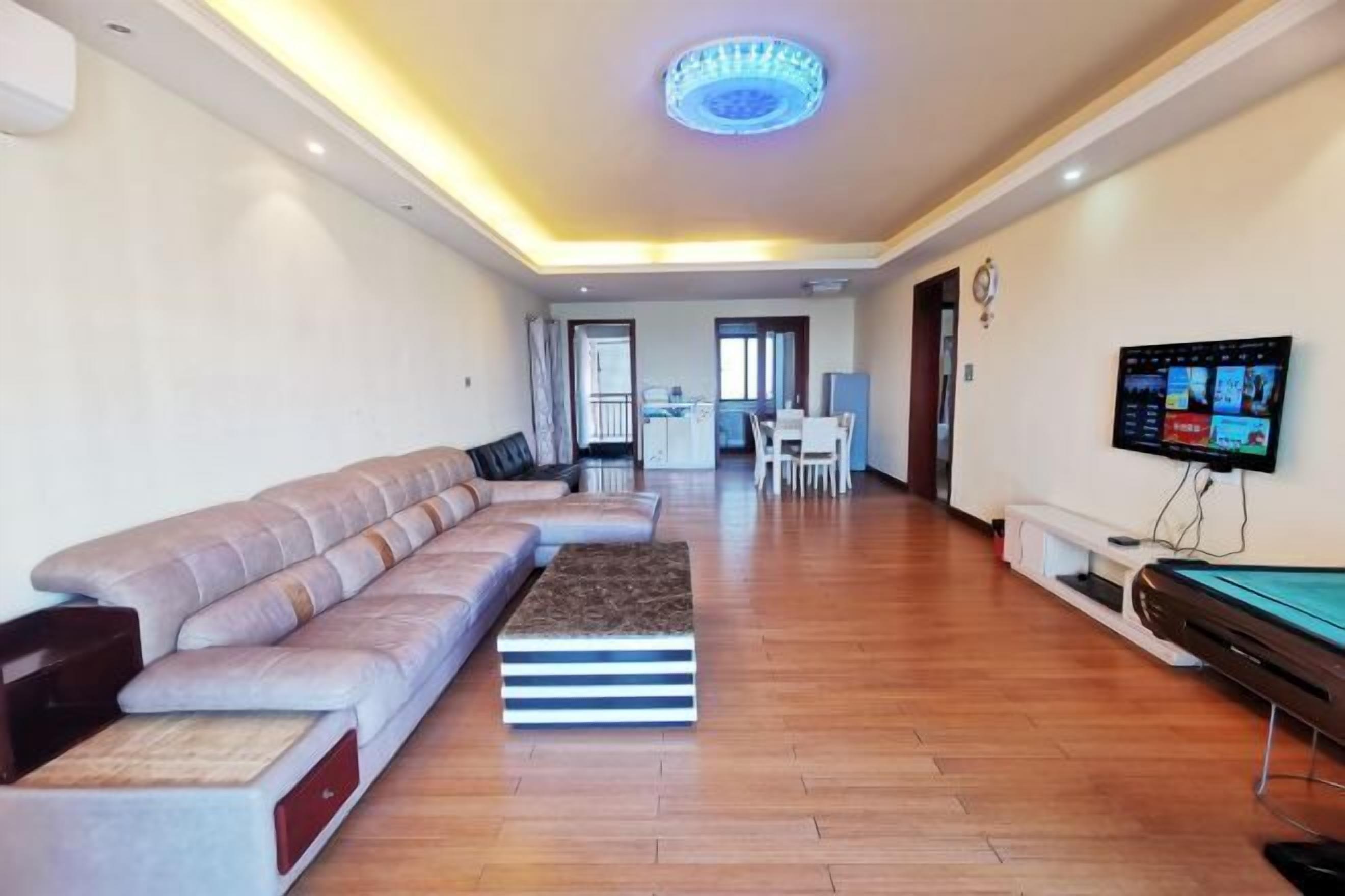 A modern living room with a sofa, a coffee table, a pool table, and a TV.