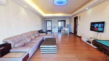 A modern living room with a sofa, a coffee table, a pool table, and a TV.