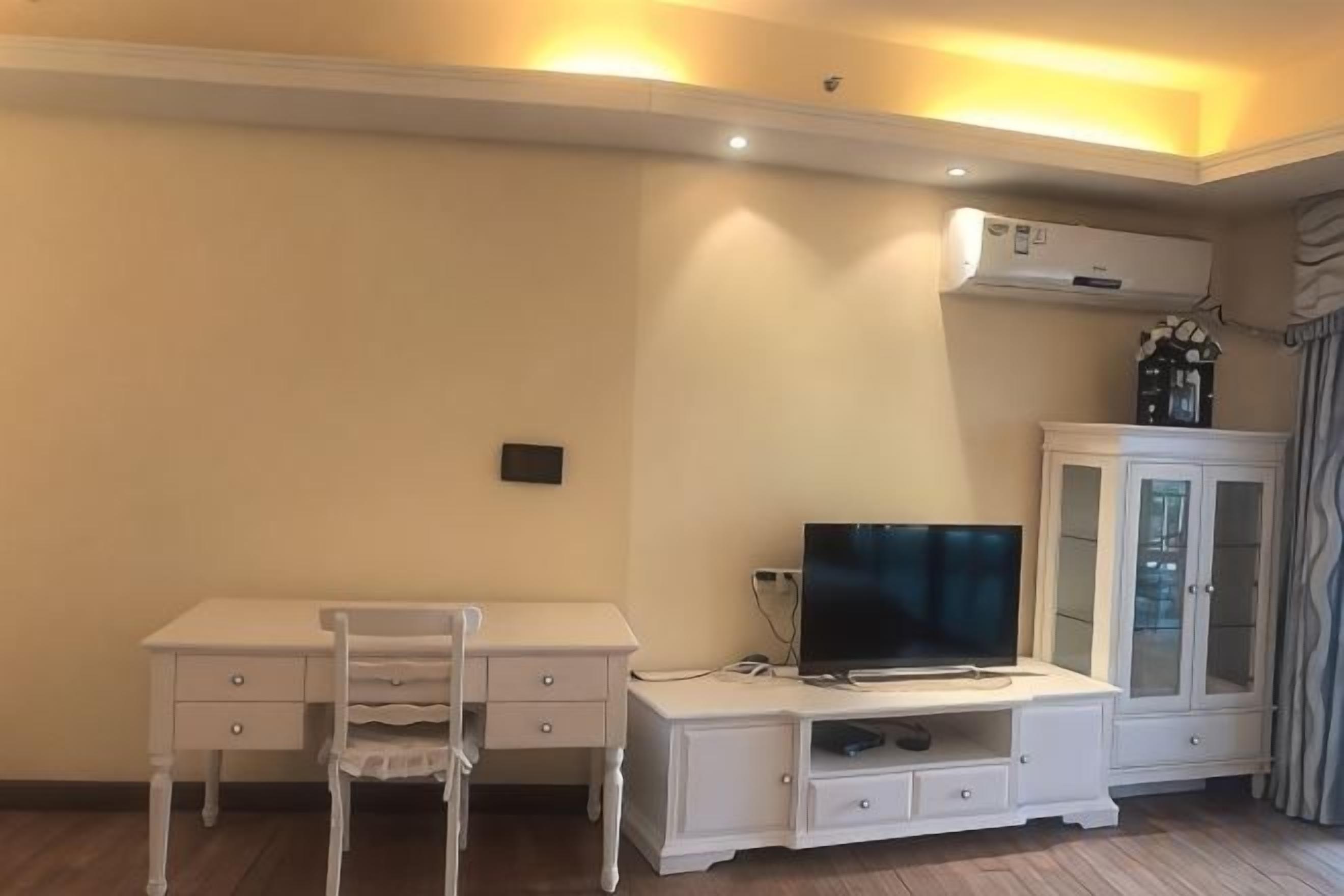 A room with a white desk, a chair, a television, and a cabinet.