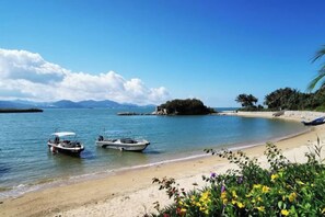 Una playa con barcos, agua cristalina y montañas a lo lejos.