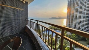 Un balcon avec vue sur la mer et une île lointaine, au coucher du soleil.