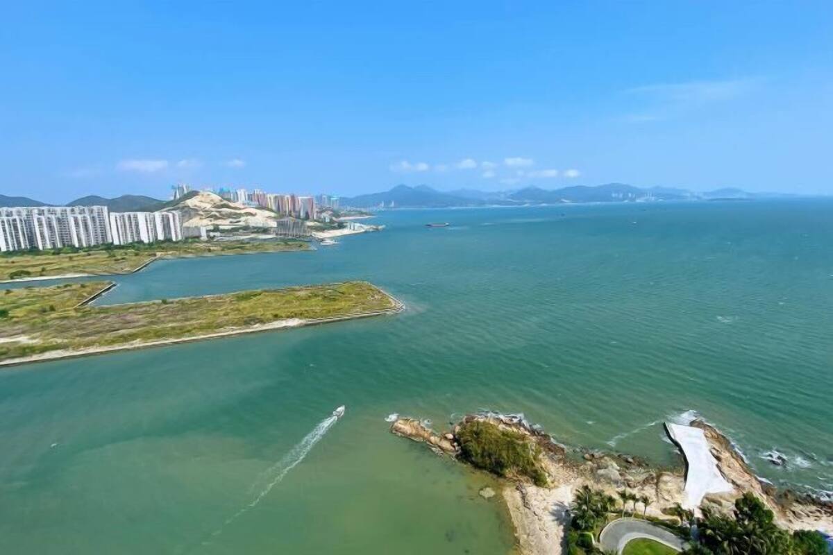 An aerial view of a coastal area with high-rise buildings, a marina, and a rocky outcrop.