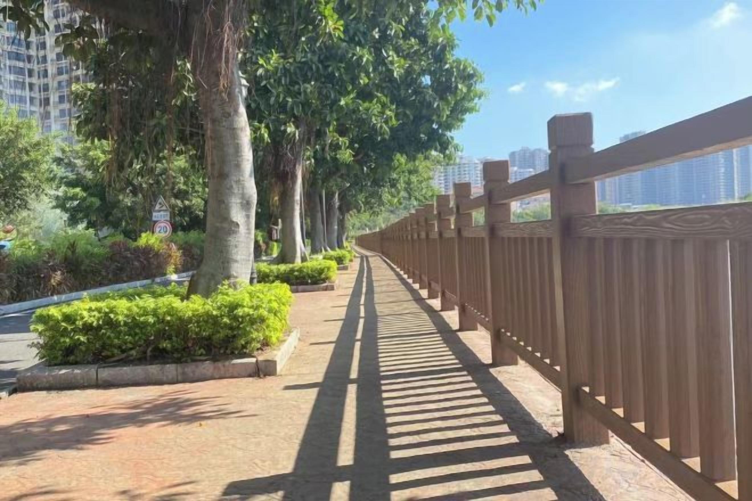 Uma trilha bordeada por árvores e cercada por uma cerca de madeira, conduzindo a um edifício com vista para edifícios altos.