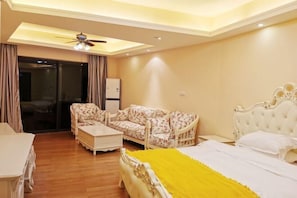 A hotel room with a bed, a sofa, a coffee table, and a ceiling fan. - Genting Coast Resort Apartment (Huidong Country Garden Shili Yintan Branch) (Huidong)