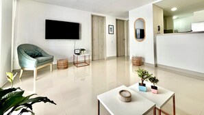 Un salon moderne doté d’un téléviseur à écran plat, d’un fauteuil confortable, d’une petite table agrémentée d’une plante, et d’un aménagement épuré et minimaliste.