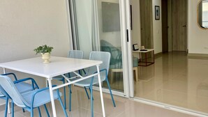 Une pièce moderne avec une table blanche et des chaises bleues, une plante en pot et une porte-fenêtre coulissante qui donne sur une autre pièce.