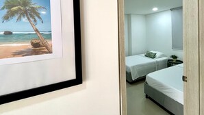Une chambre avec deux lits, un tableau encadré représentant une plage et un miroir qui reflète la pièce.