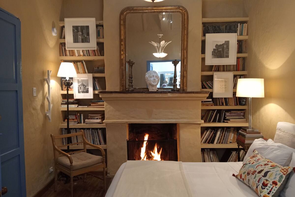 Ein Schlafzimmer mit Kamin, Bücherregalen, einem Bett und einem Sessel.