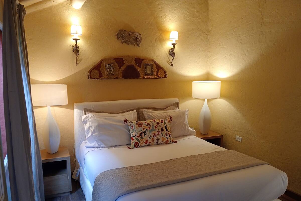 Ein Hotelzimmer mit einem großen Bett, zwei Nachttischlampen, einem dekorativen Wandbild über dem Bett und einem Holznachttisch.