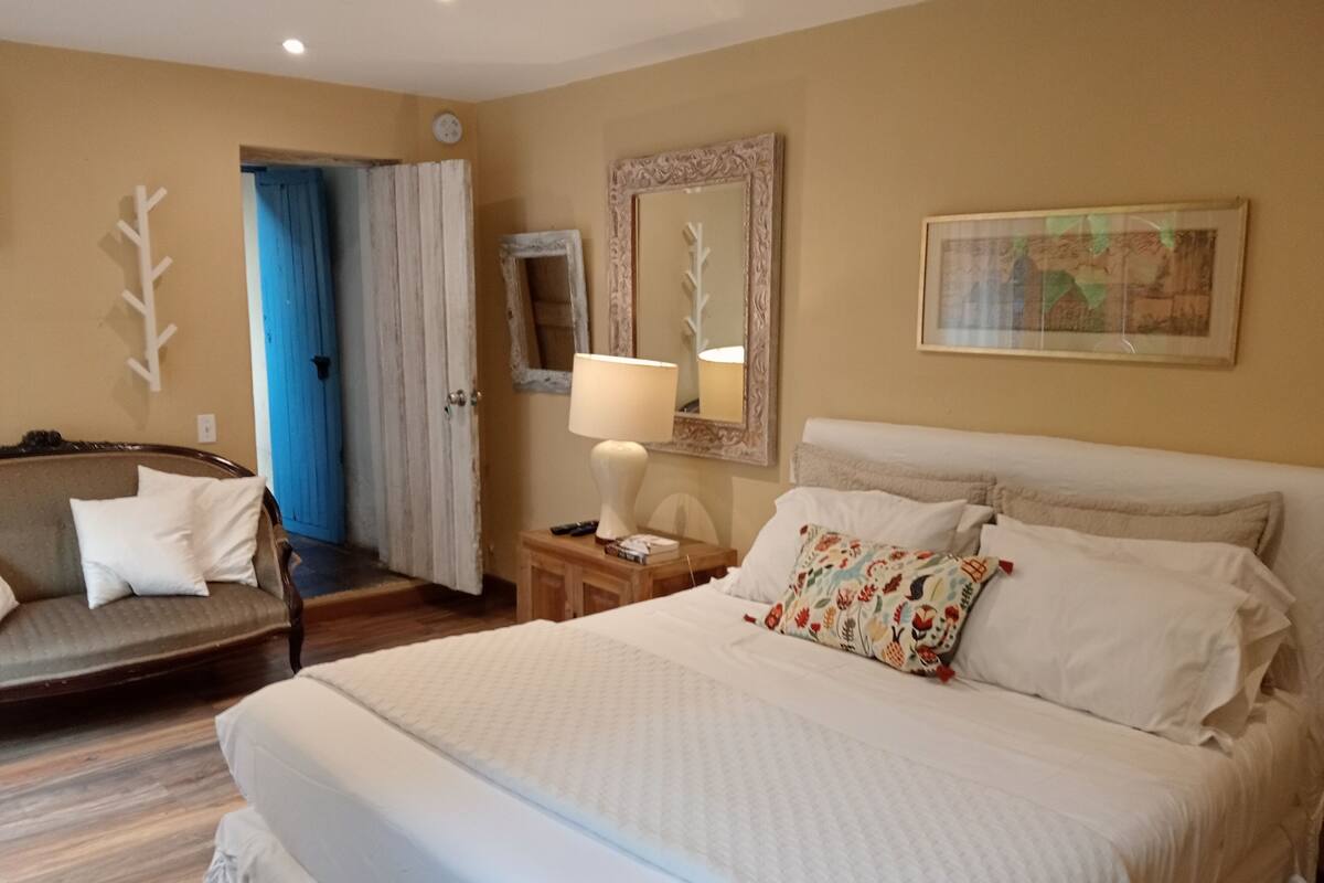 Ein Hotelzimmer mit Bett, Stuhl, Lampe, Spiegel und einem Bild an der Wand.