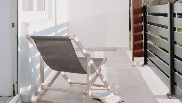 A balcony with a wooden chair and a table, a glass of water, and an open book.