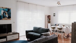 A modern living room with a sofa, a TV, and a dining area with a table and chairs.